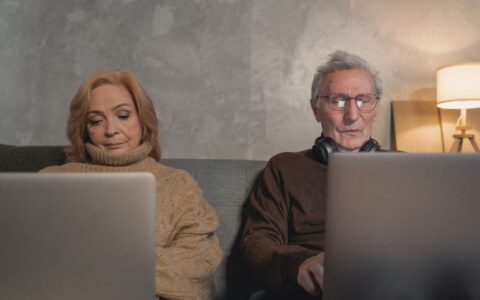 Elderly couple engaging with technology on their laptops at home, showcasing modern senior lifestyle.