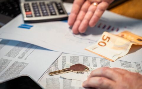 Hands examining financial documents, a 50 euro note, and a key, suggesting investment or real estate themes.