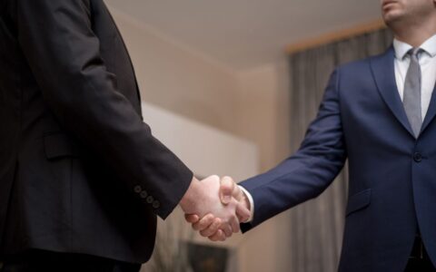 Two businessmen in suits shaking hands, emphasizing trust and partnership indoors.