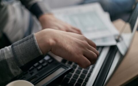 Close-up of hands calculating finances with a laptop and paperwork.