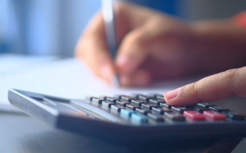 A close-up image of hands working on a calculator and writing, representing budgeting and financial planning.
