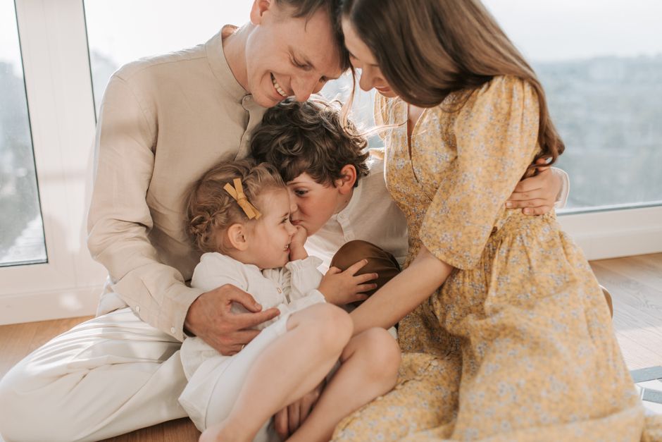 A happy family of four sitting together and sharing a loving moment indoors.