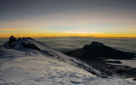 Majestic sunrise view from a snowy peak with vibrant sky colors contrasting the rugged terrain.