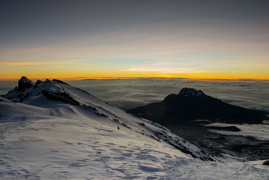 Majestic sunrise view from a snowy peak with vibrant sky colors contrasting the rugged terrain.