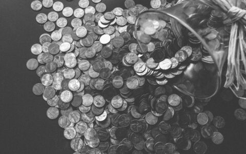 Monochrome image of coins spilling from a glass jar, symbolizing wealth and savings.
