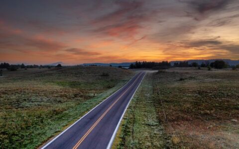 An empty rural road in West Newton, MN at dusk with vibrant sky and open fields.