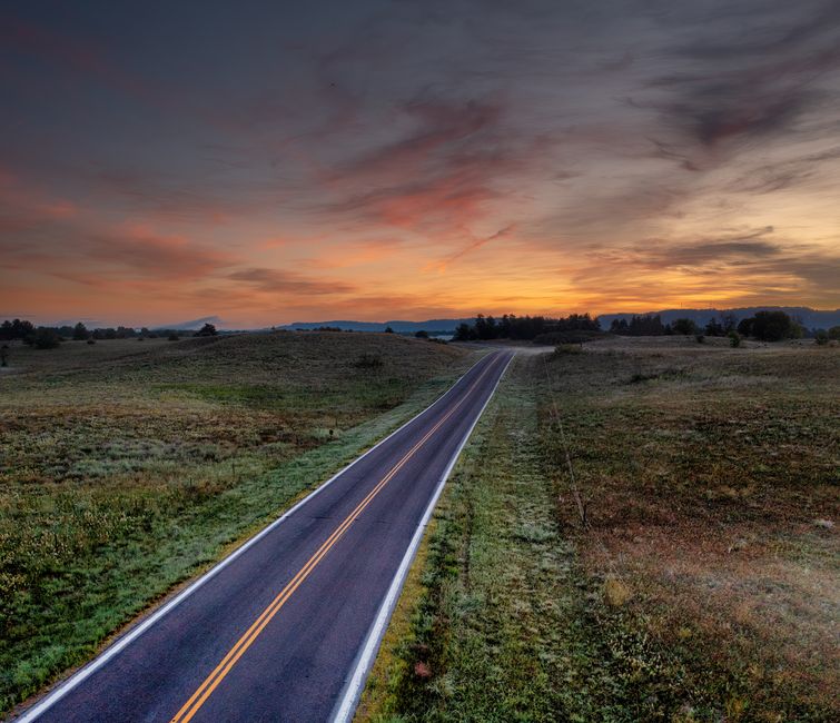 An empty rural road in West Newton, MN at dusk with vibrant sky and open fields.