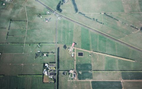 Aerial shot showcasing expansive green farmland with field boundaries and rural structures.